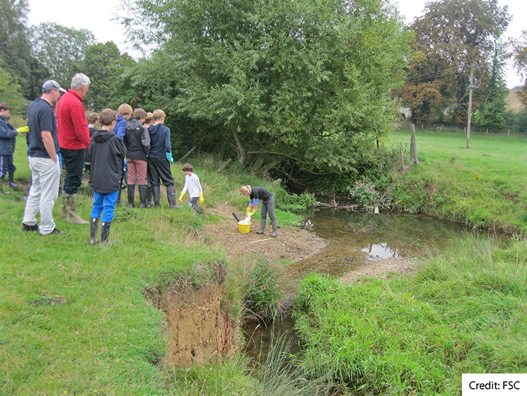 A group of students with their teacher on a riverbank carrying out fieldwork together